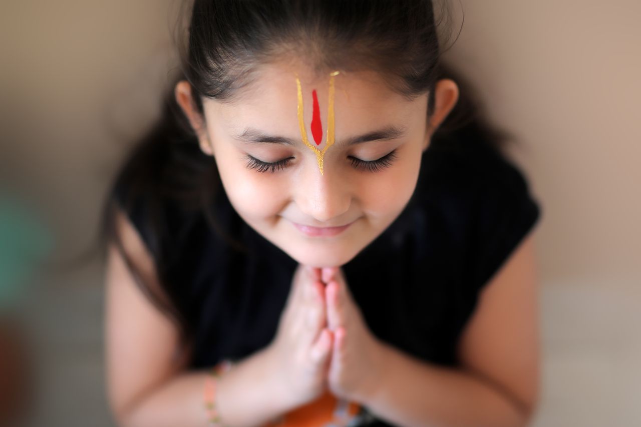 A young girl in Bhavnagar, India, prays with closed eyes and hands joined, displaying innocence and devotion.